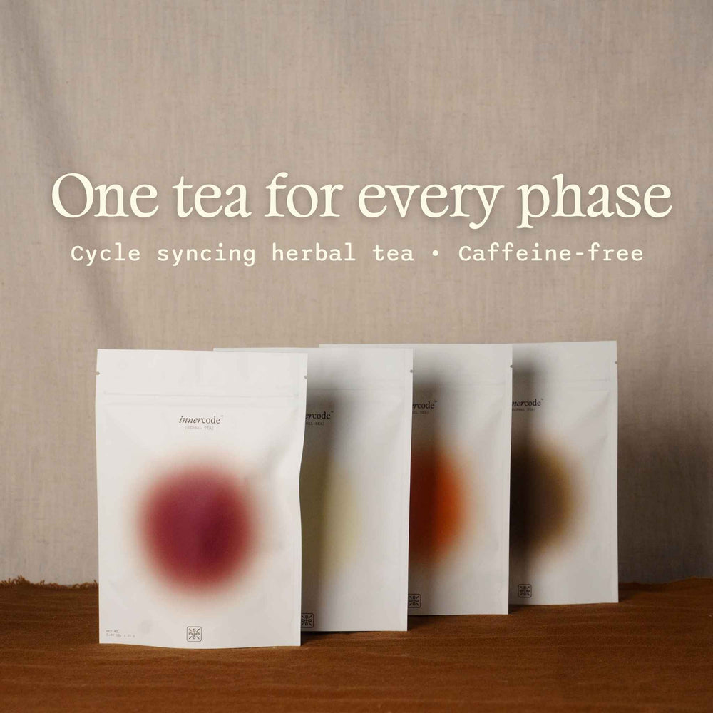 Four white stand-up pouches of Inner Code Cycle Syncing Herbal Tea arranged in a row on a wooden surface against a beige fabric backdrop, with the text 'One tea for every phase' displayed above.